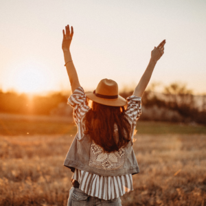 Woman walks through fields has her arms up with joy