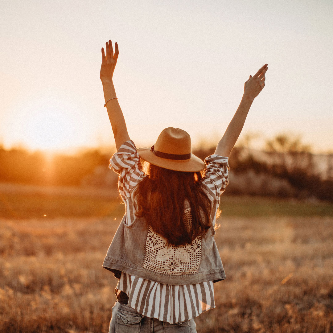 Woman walks through fields has her arms up with joy